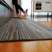 料理をしている飼い主とキッチンマットにいる子猫