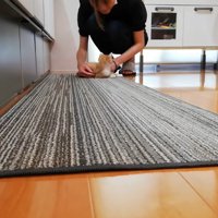 料理をしている飼い主とキッチンマットにいる子猫