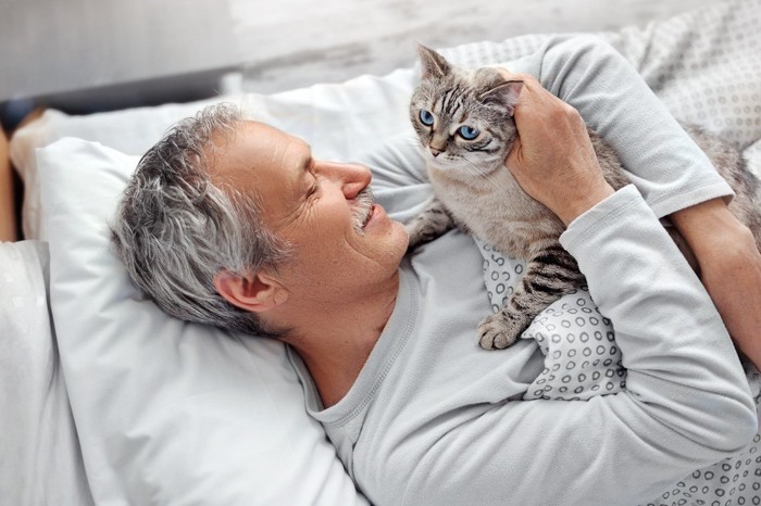 寝そべる男性の上に乗っかる猫