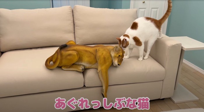 ソファの上にライオンの置物の匂いを嗅ぐ猫