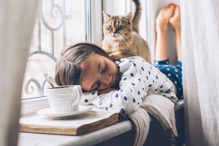 うつ伏せで眠る女の子の背中に乗る子猫