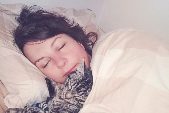 女性の顔のそばで眠る猫