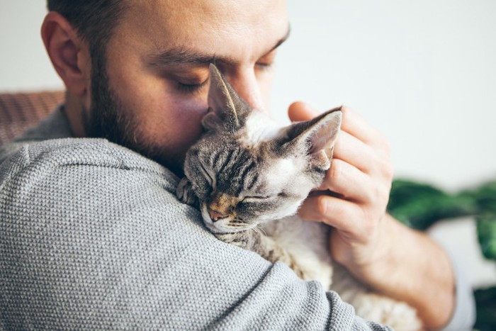 目を閉じて男性に抱きしめられている猫