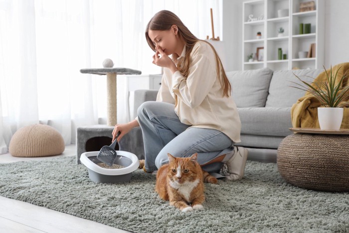 鼻をつまんでトイレ掃除をする女性と猫