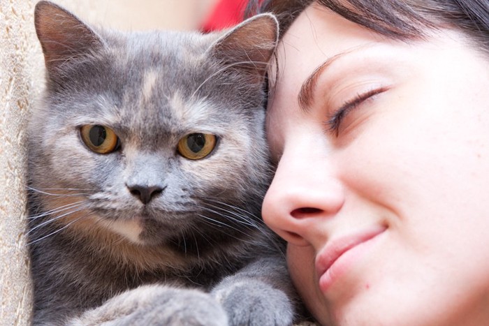 目を閉じて猫の顔に顔を近づける女性