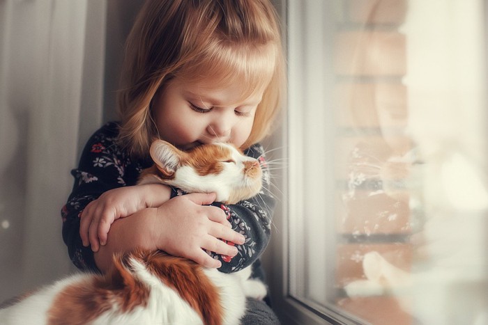 小さい子どもに抱きしめられる猫