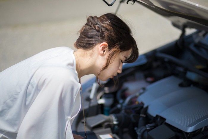 車のエンジンルームをのぞく女性