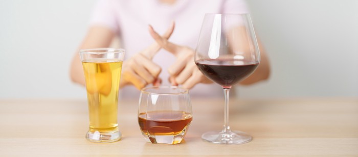 お酒のグラスとバツ印を作っている女性の手