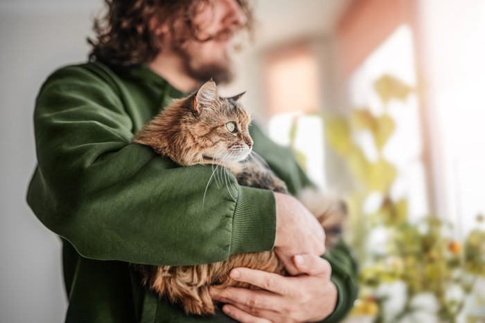 猫を抱いて外を見る男性
