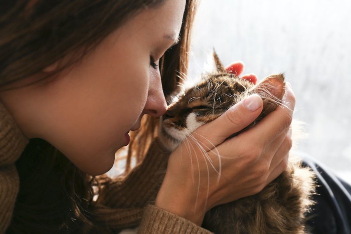 猫の顔を両手で包んで顔を近づける女性