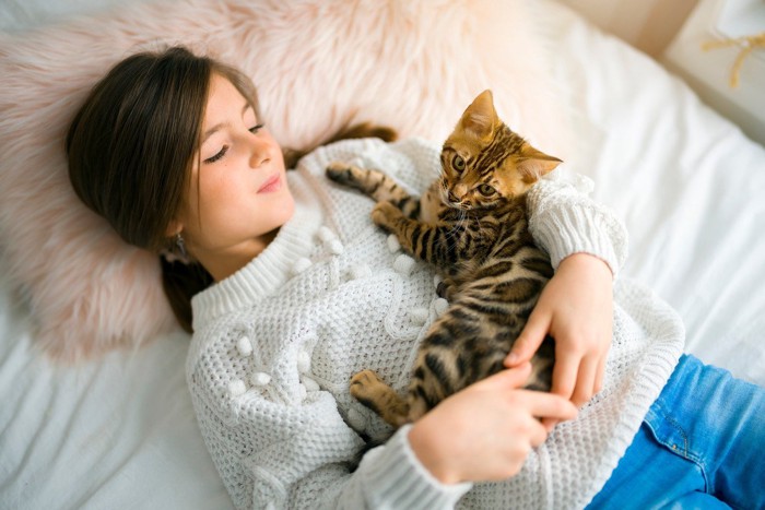 ベッドの少女の上で困惑する子猫