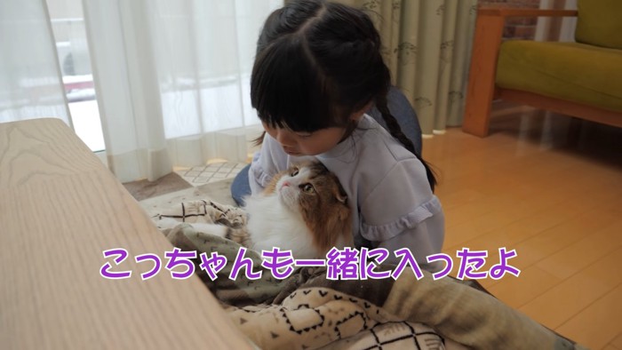 猫を抱っこしてこたつに入るこども