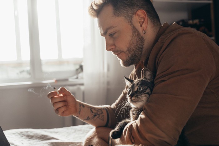 たばこを吸う男性に抱かれた猫