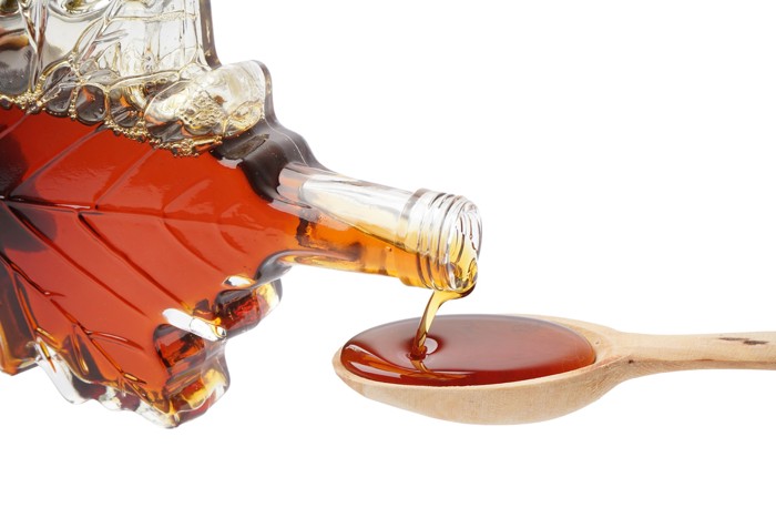 ボトルからスプーンにメープルシロップを注いでいる光景