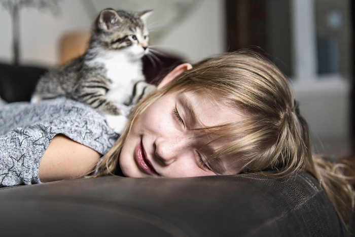 うつ伏せに寝る飼い主の背中に乗る猫