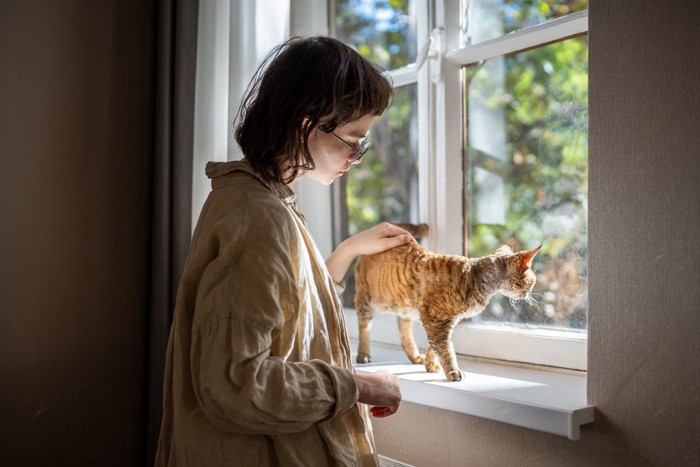 窓辺でたたずむ女性と猫