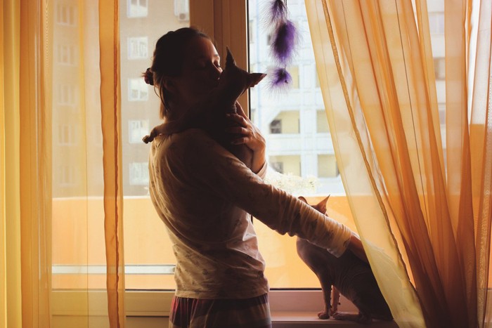 猫を抱きながらもう1匹の猫を撫でる女性