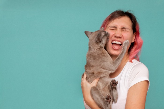 女性の顔を噛む猫