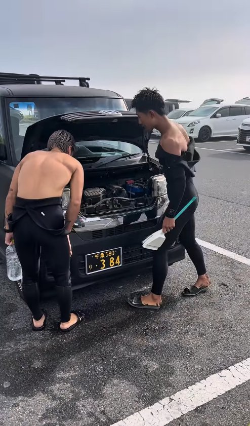 エンジンルームを覗き込んでいる2人のサーファー