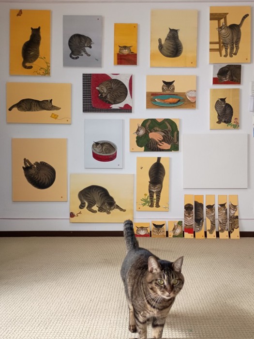 壁に猫の絵が飾ってある、手前にはキジトラ猫