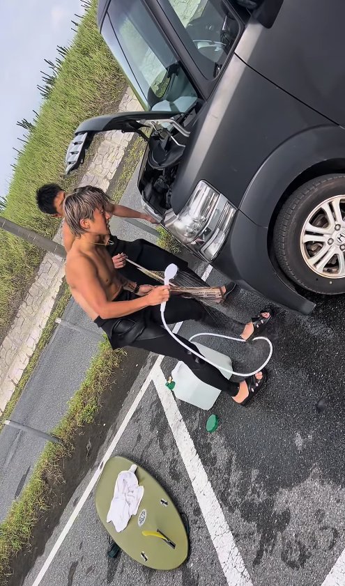 シャワーを持ってエンジンルームを覗き込むサーファー