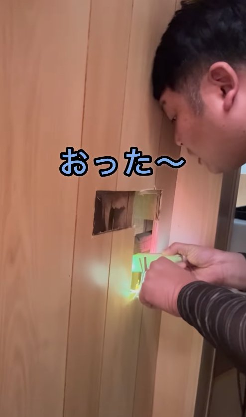 壁に開いた穴を覗き込む男性