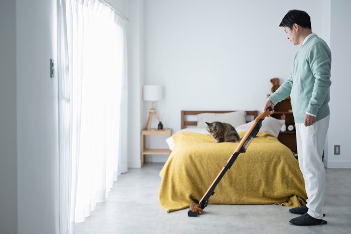 掃除機をかける男性と猫