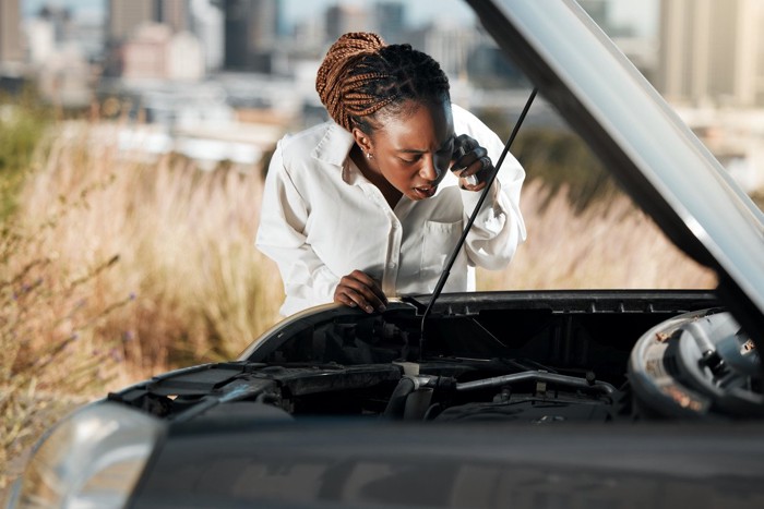 車のエンジンルームをのぞきながら電話する女性