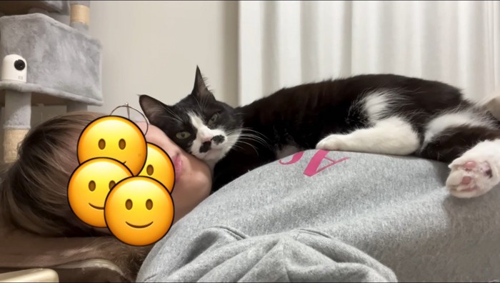 横になっている女性の顔に頭を乗せるハチワレ猫