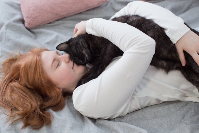 寝ている女性に抱きしめられている猫