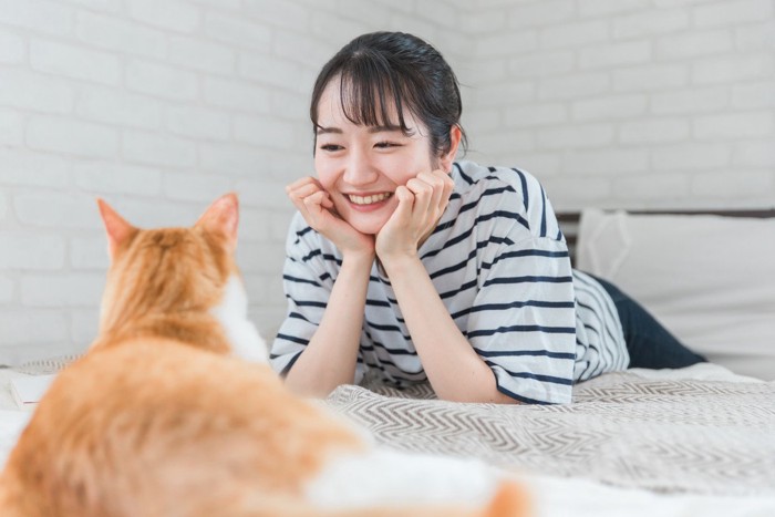 うつ伏せで見つめ合う猫と女性