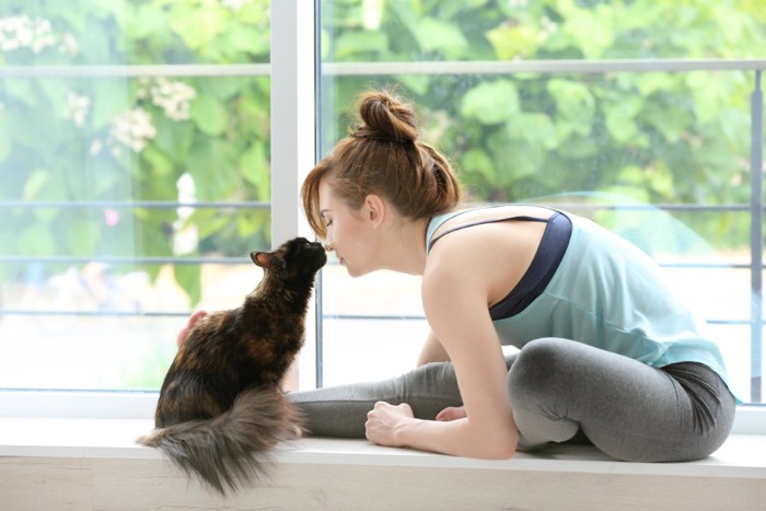 窓辺で鼻チューをする猫と女性