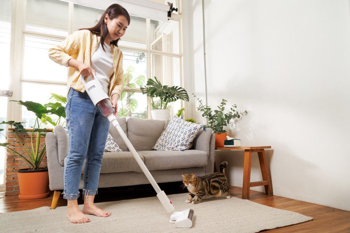 部屋に掃除機をかける飼い主と猫
