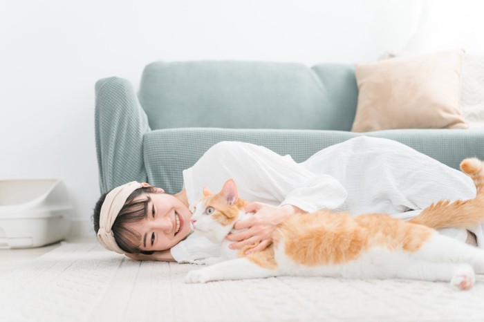 床の上で横たわり、猫と遊ぶ女性