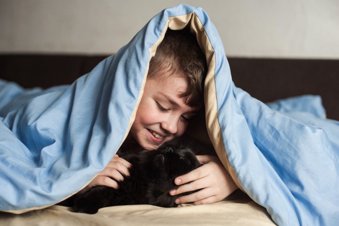 ふとんの中で黒猫と遊ぶ少年
