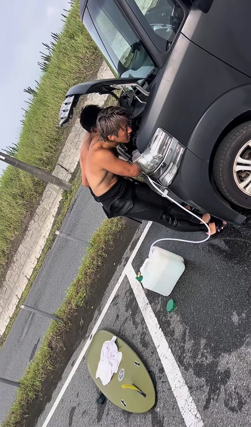 エンジンルームに顔を近づけてシャワーをかけているサーファー