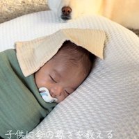 クッションの上にアゴを乗せて、赤ちゃんを見つめる白い犬