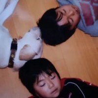 頭をくっつけ合って寝転がる犬と2人の男の子