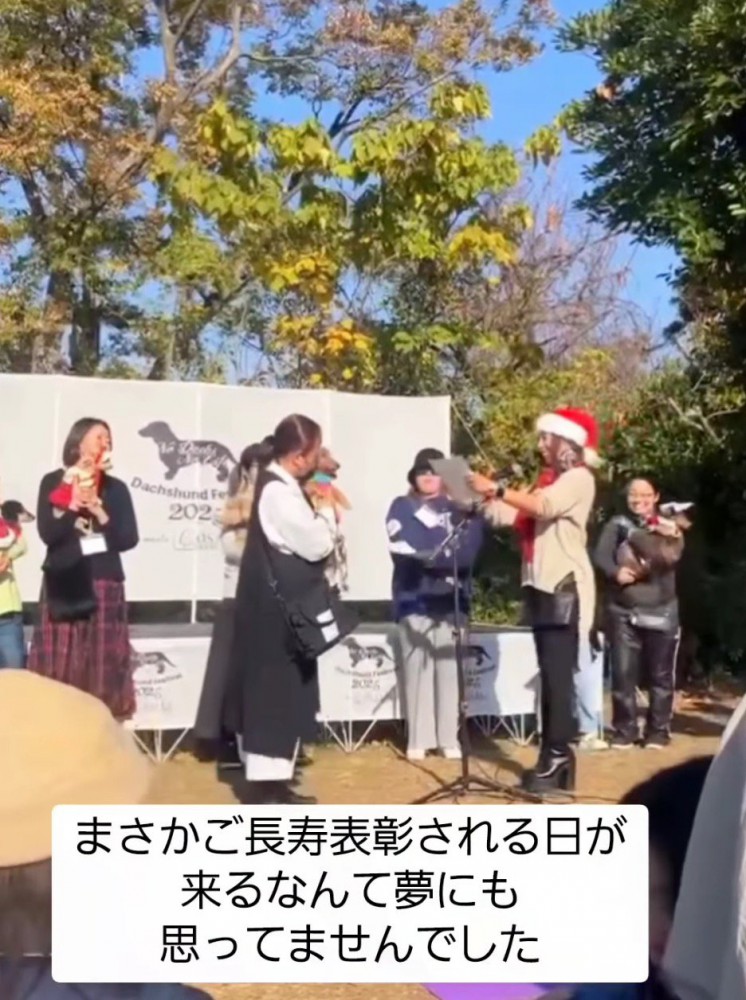 賞状を読み上げる女性の前に立つ飼い主と犬