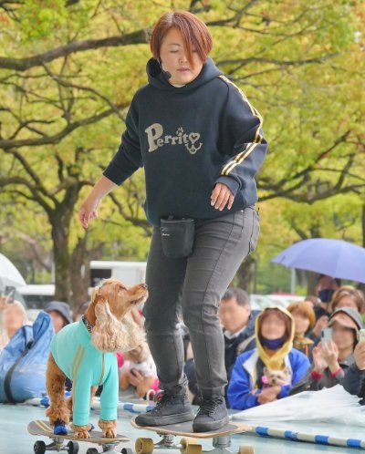 トレーナーと一緒にスケボーをする犬