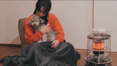 ストーブの前で犬を抱いて温まる飼い主
