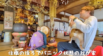 住職がお経を唱える後ろで妹犬を宥める男性