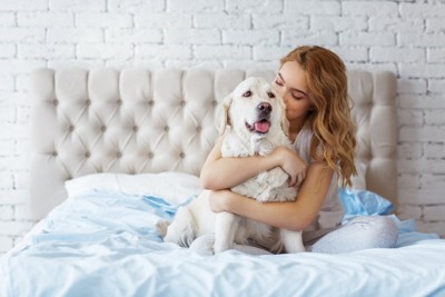 ベッドの上で愛犬を抱きしめる女性