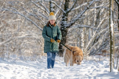 雪の中を散歩する女性と犬