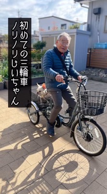 電動式三輪車に跨がってカメラに視線を送る年配男性