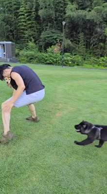 男性の後ろから走ってくる黒い犬