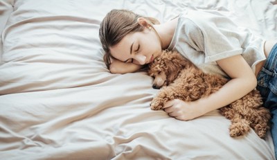 ベッドで添い寝する女性と犬