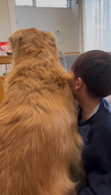 座っている犬にもたれかかっている男の子の後ろ姿