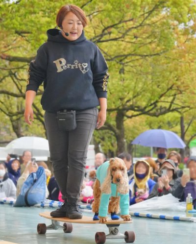 トレーナーと一緒にスケボーをする犬