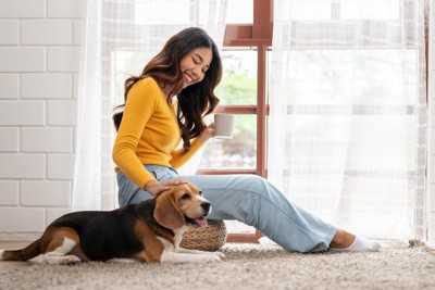 カップを持つ女性とそばでフセする犬